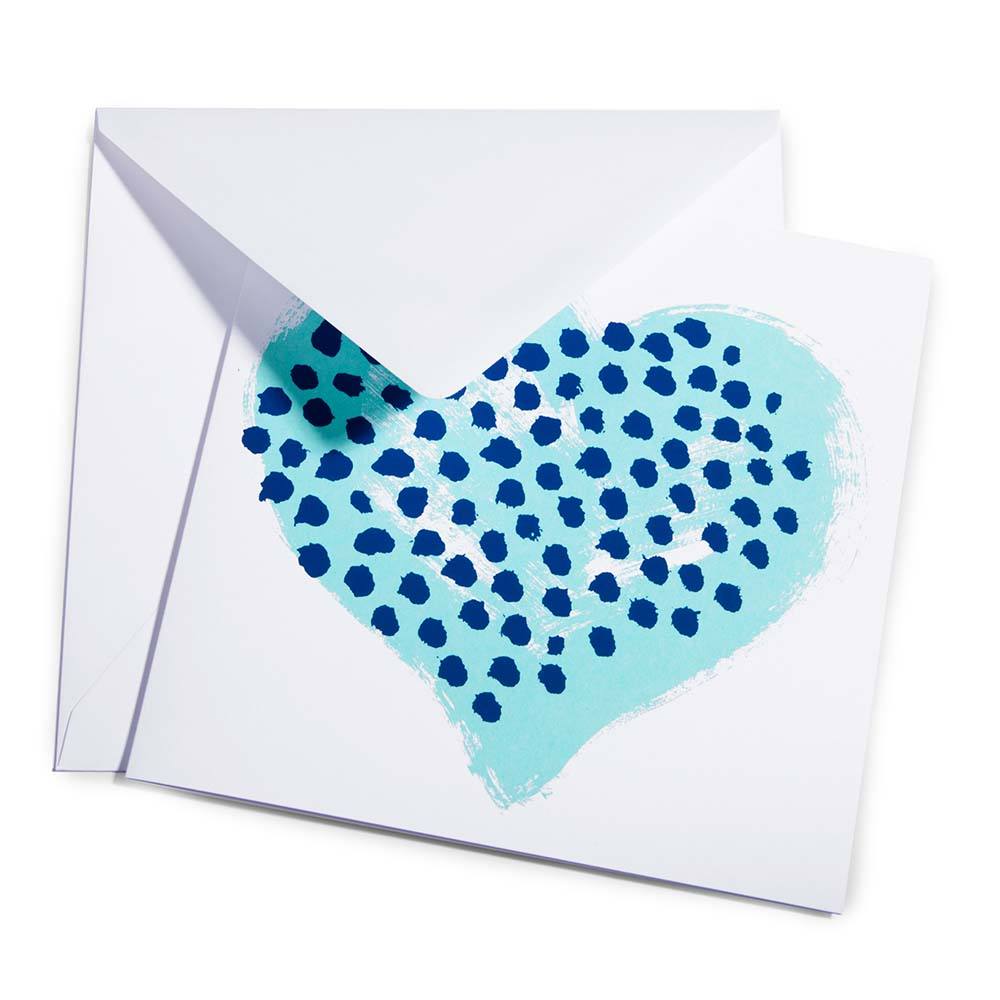 Greeting card with a minimalist design, featuring a large turquoise heart filled with dark blue hand-painted dots, shown partially tucked into a white envelope at a slight angle.