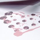 Greeting card with a minimalist design, featuring a hand-stamped heart made of soft pink and muted purple dots, shown in a close-up view with gentle shadows and the envelope partially open above it.