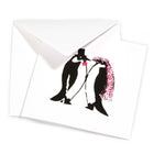 A folded greeting card shown with its envelope, featuring the same penguin wedding illustration centered on the front.