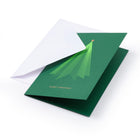 A green Christmas card with a stylized tree design and the words "Merry Christmas," partially inserted into a white envelope on a white background.