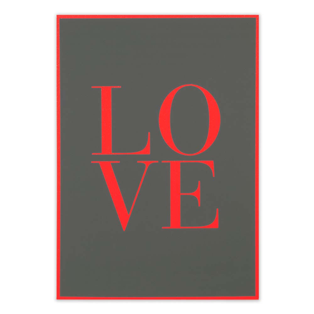 A flat-lay view of a dark grey greeting card featuring the word “LOVE” in large red letters, framed by a thin red border against a neutral background.