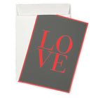 A dark grey greeting card shown at a slight angle, with the word “LOVE” printed in bold red letters and a matching red border, partly pulled from a white envelope.