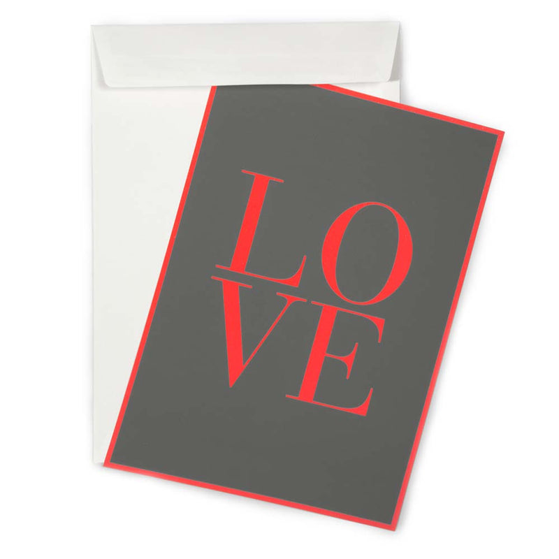 A dark grey greeting card shown at a slight angle, with the word “LOVE” printed in bold red letters and a matching red border, partly pulled from a white envelope.