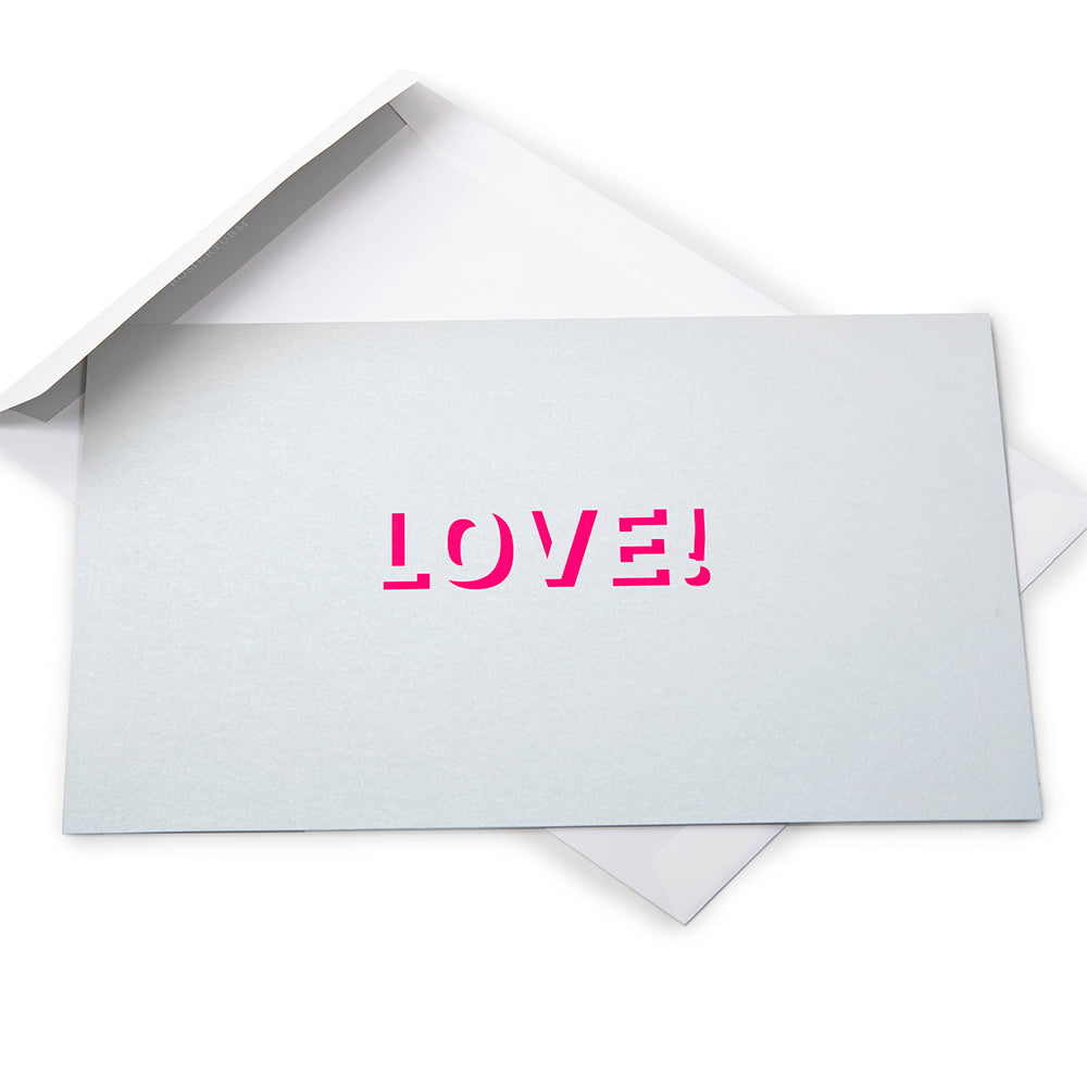 Silver greeting card with a metallic finish and the word “LOVE!” cut out in bright pink, shown with a white envelope behind it.