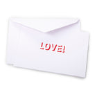 Greeting card with a minimalist design, featuring the word “LOVE!” cut out in bold red lettering on a crisp white folded card, partially tucked into a matching envelope and photographed at a slight angle with soft studio lighting.
