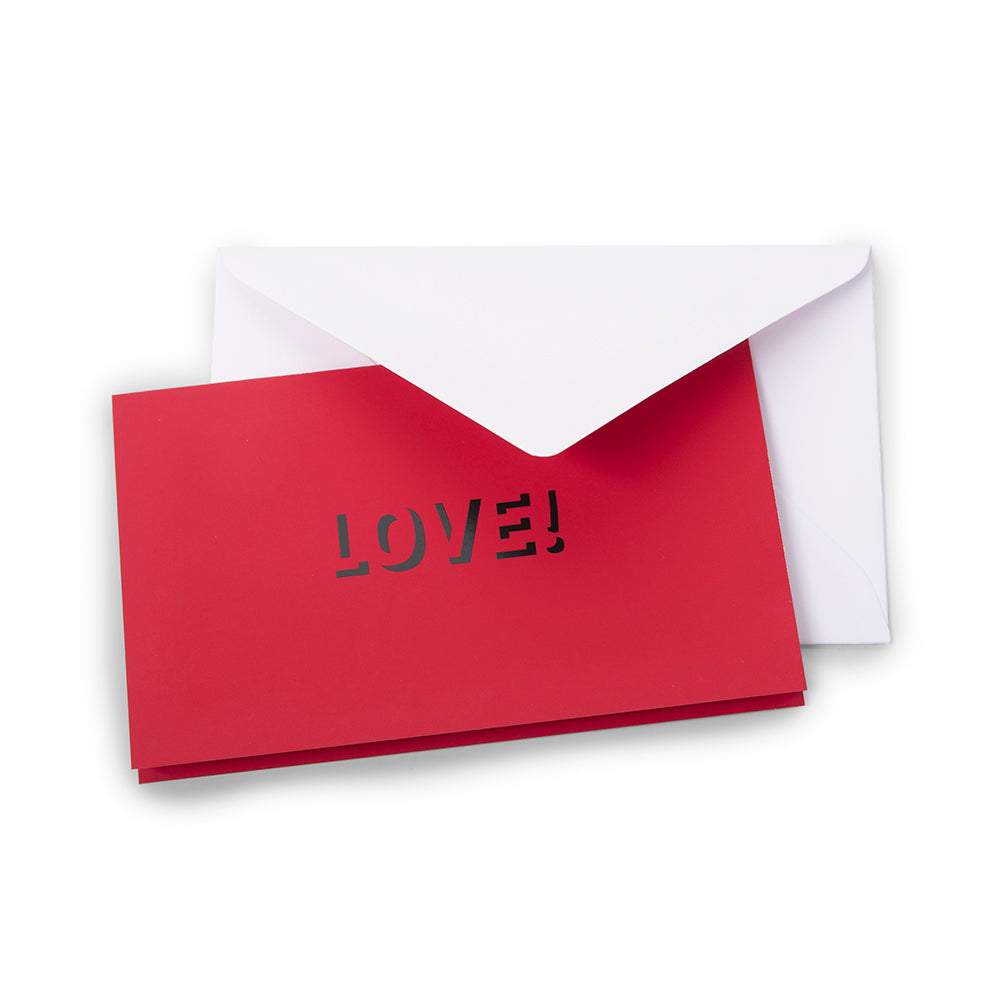 A red greeting card partly pulled from a white envelope, with the word “LOVE!” cut out on the front.