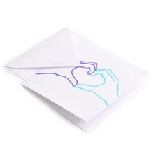 Greeting card with a simple continuous-line illustration of two hands forming a heart, drawn in purple and turquoise on a clean white background, shown with a white envelope.