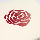 Close-up of a hand-printed red rose motif on textured ivory paper, highlighting the uneven ink and organic paper surface.