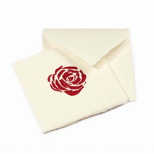 Greeting card with deckled edges, showing a single deep red rose printed at the center on warm ivory paper, with the matching envelope placed behind it.