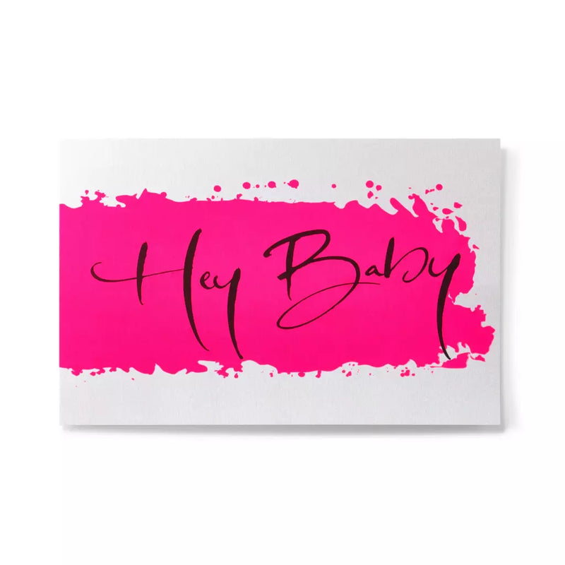 A flat white greeting card with a vivid hot-pink brushstroke centered across the surface, accented by the words “Hey Baby” written in elegant black calligraphy.