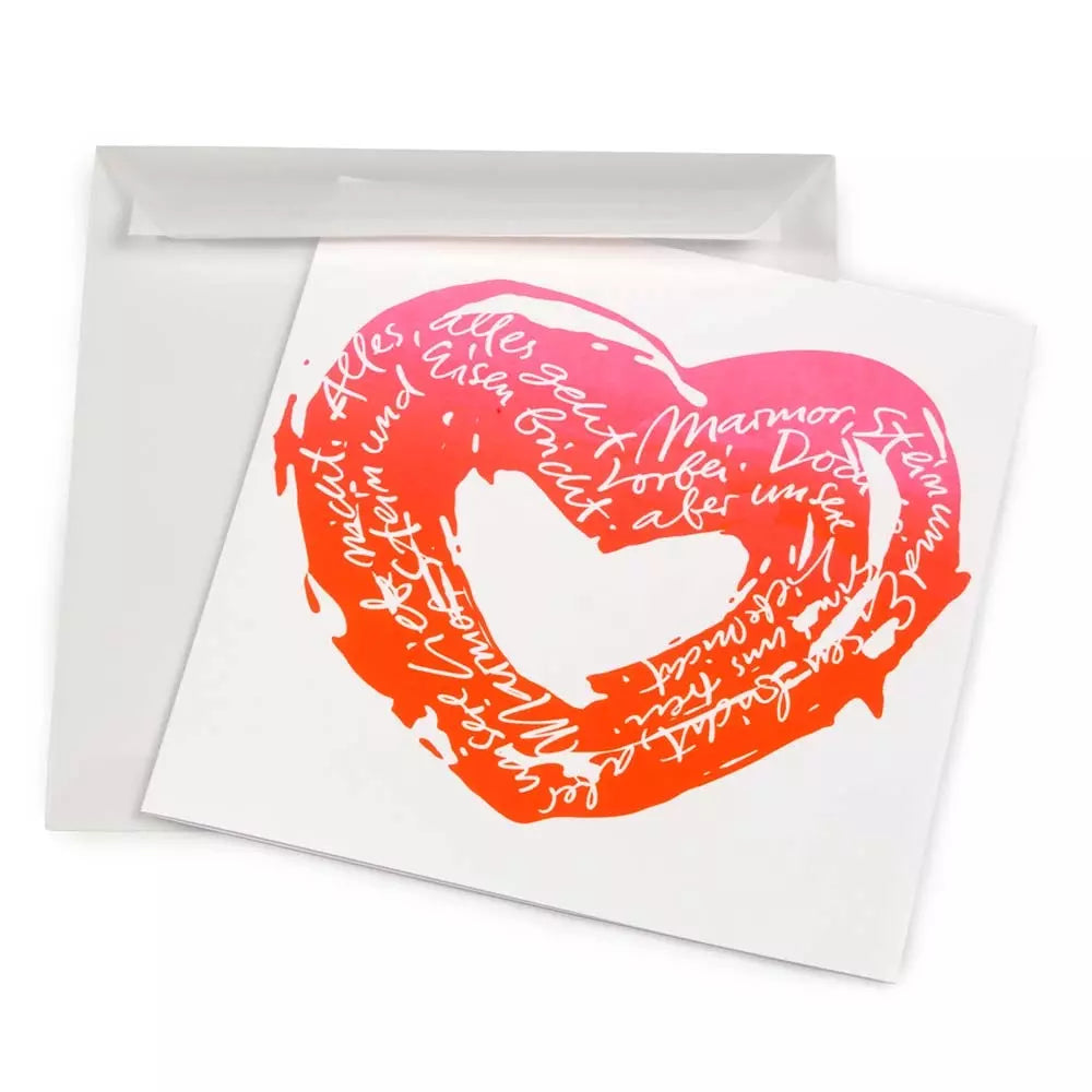 A white greeting card shown slightly angled, featuring a hand-painted heart in a vivid pink-to-orange gradient, filled with flowing handwritten text in white and paired with a matching white envelope.