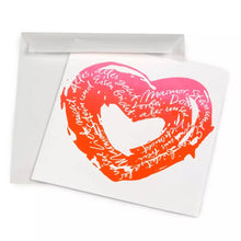 A white greeting card shown slightly angled, featuring a hand-painted heart in a vivid pink-to-orange gradient, filled with flowing handwritten text in white and paired with a matching white envelope.