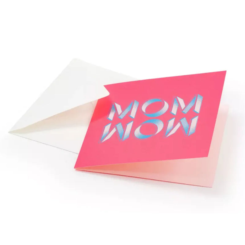 A playful greeting card with a textured pink background, showcasing “MOM WOW” in chunky, stylized letters with a light blue and white gradient and subtle halftone detailing, tucked into a white envelope.