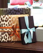 Stacked gift boxes featuring leopard print, solid colors, and satin ribbons in soft blue and warm orange tones, arranged on a wooden surface in natural light.