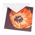 A greeting card partially tucked into a white envelope, showcasing a striking oversized poppy illustration with painterly textures and high-contrast colors on a dark backdrop.