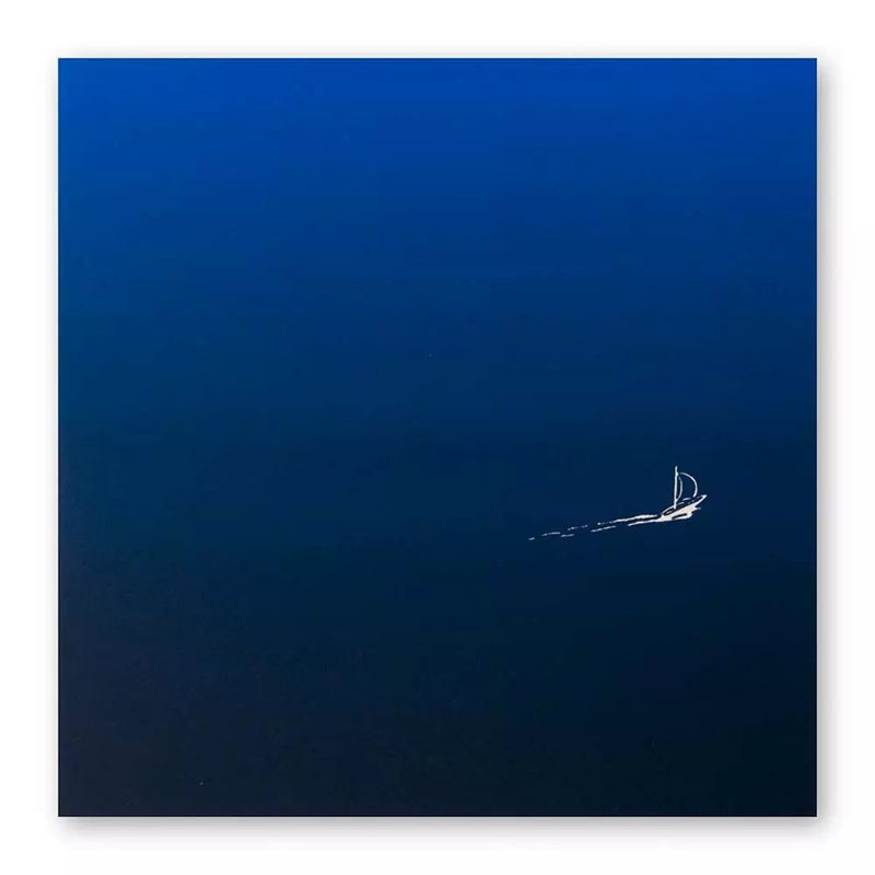 A minimalist greeting card with a deep blue gradient background, featuring a tiny white sailboat leaving a delicate trail across the open water.