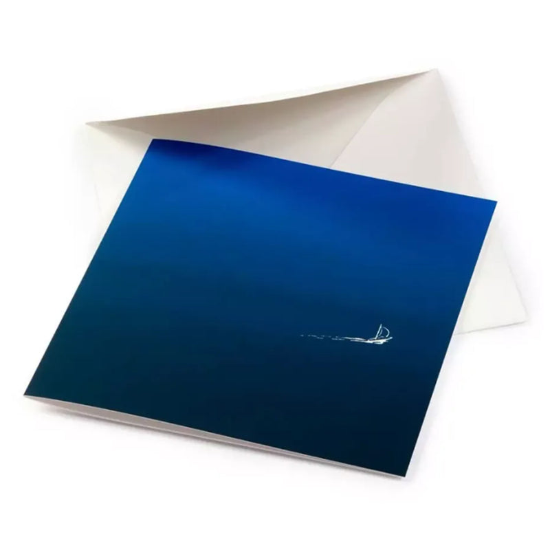 A greeting card partly tucked into a white envelope, showing a vast blue gradient surface with a small white sailboat drifting quietly across it.