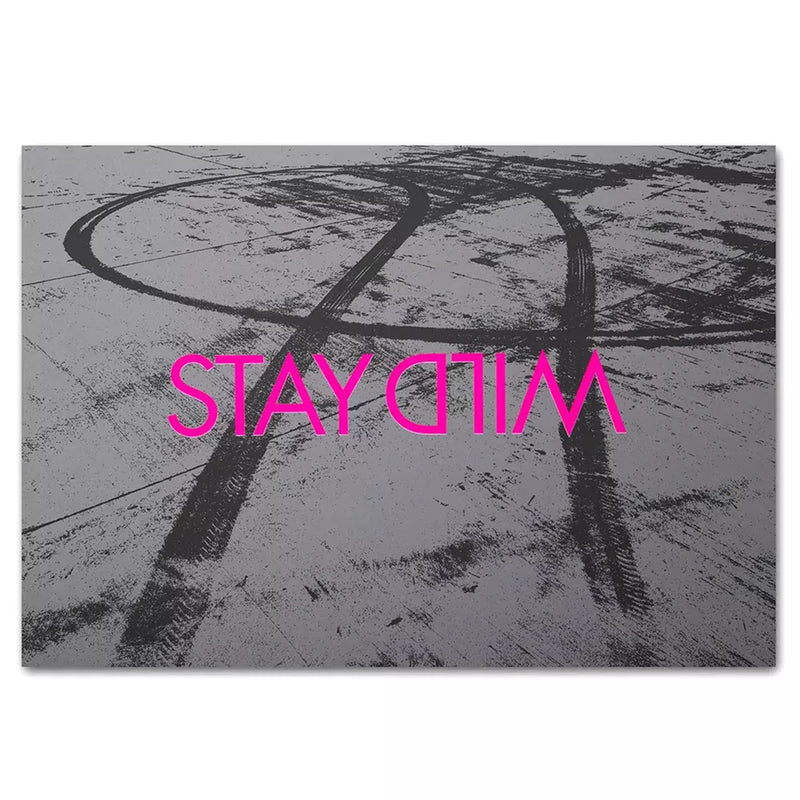 A rectangular greeting card with a monochrome background of tire marks on a rough surface, featuring the words “STAY WILD” in bold bright pink lettering.