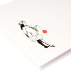 A close-up of a white Christmas card with a black illustration of a noble figure holding a large red Christmas ornament.