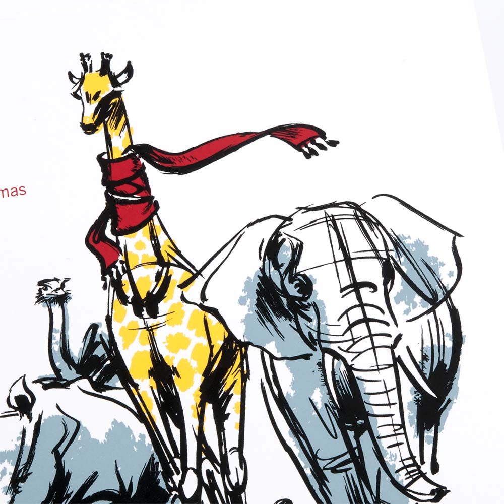 A close-up of a white Christmas card with an illustrated giraffe wearing a red scarf, walking alongside an elephant and a rhinoceros, with the text “Coming home for Christmas.”