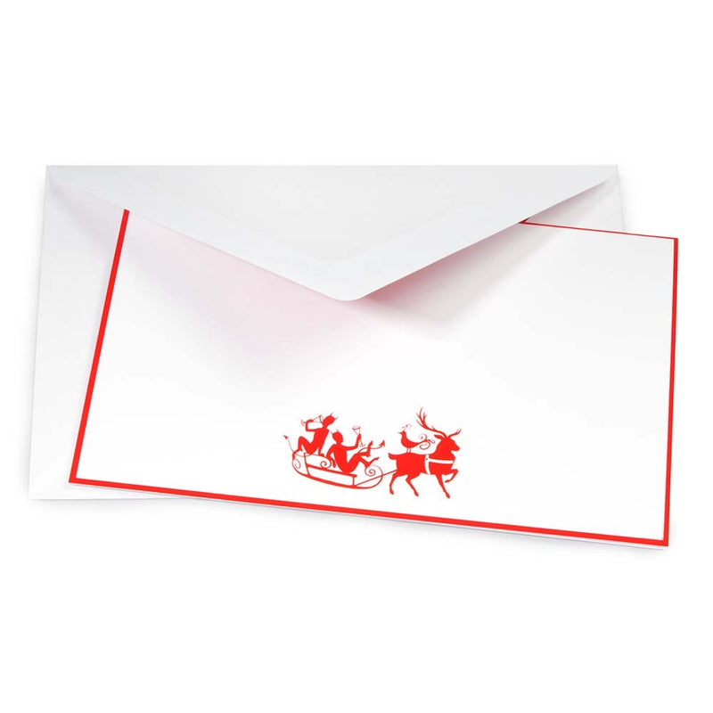 White Christmas card with red border, featuring a playful illustration of two reindeer pulling a sleigh with characters raising glasses, accompanied by a matching envelope.
