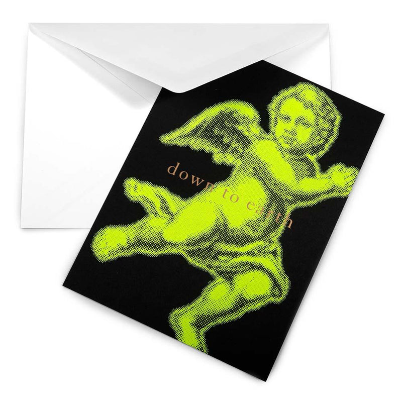 Christmas card with a bold neon yellow angel illustration on a black background, accompanied by the text 'down to earth,' paired with a white envelope.