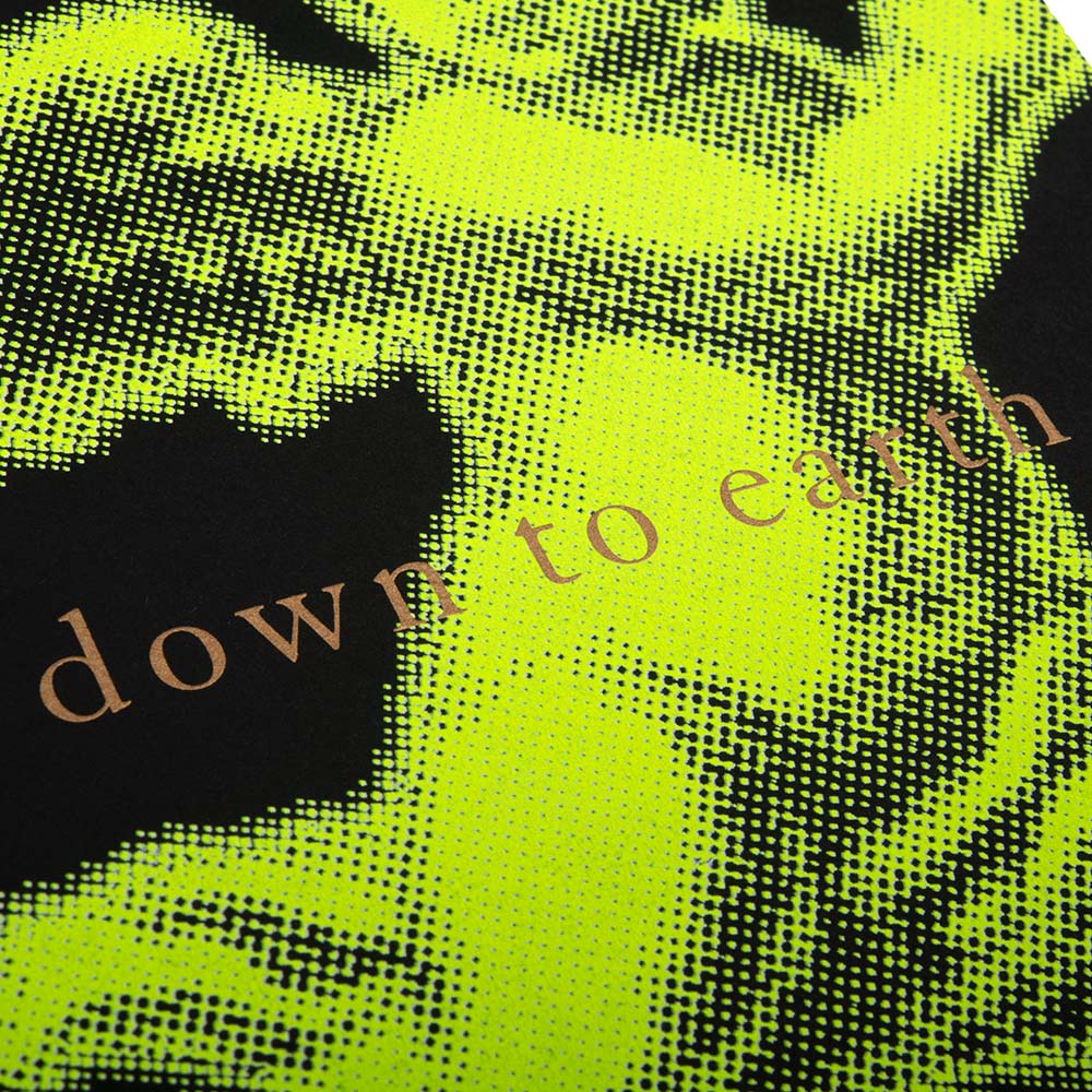 A close-up of a Christmas card with a bold neon yellow angel illustration on a black background, accompanied by the text 'down to earth'.