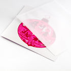 Christmas card with a bright pink ornament illustration filled with silhouettes of festive figures, animals, and decorations, paired with a translucent envelope.