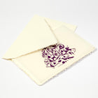 A cream-colored Christmas card with deckle edges, printed with a detailed purple ornamental design featuring festive silhouettes, paired with a cream envelope.