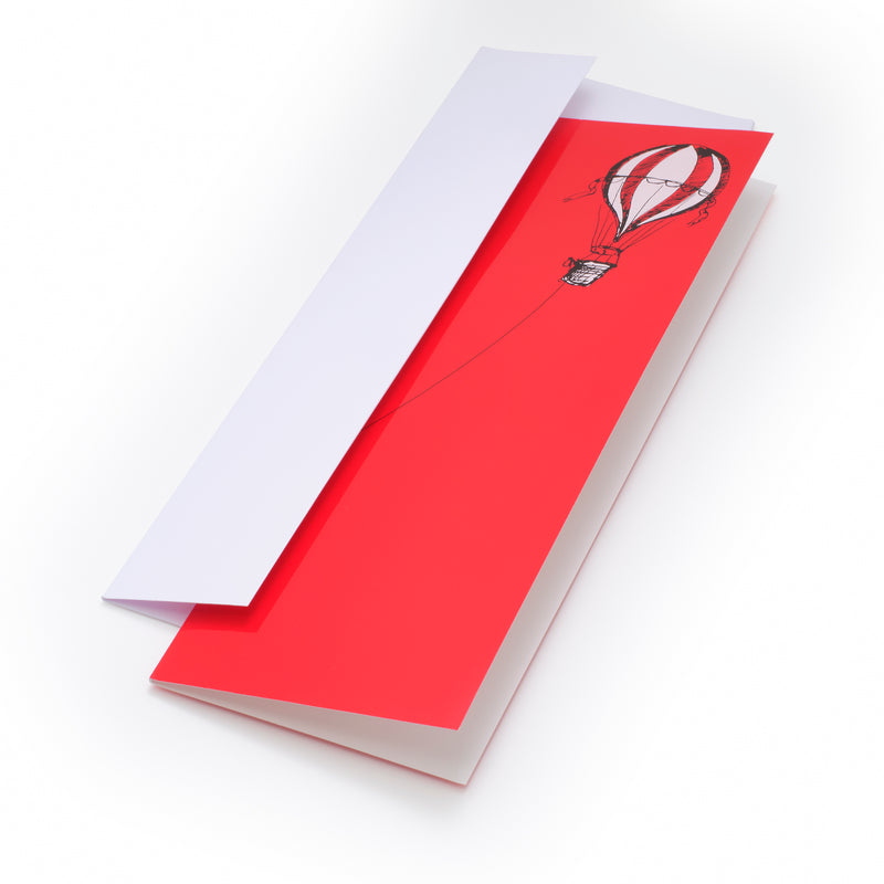 Christmas card with a bold red background, featuring a black illustration of a hot air balloon on the right, with a long rope extending left, paired with a white envelope.