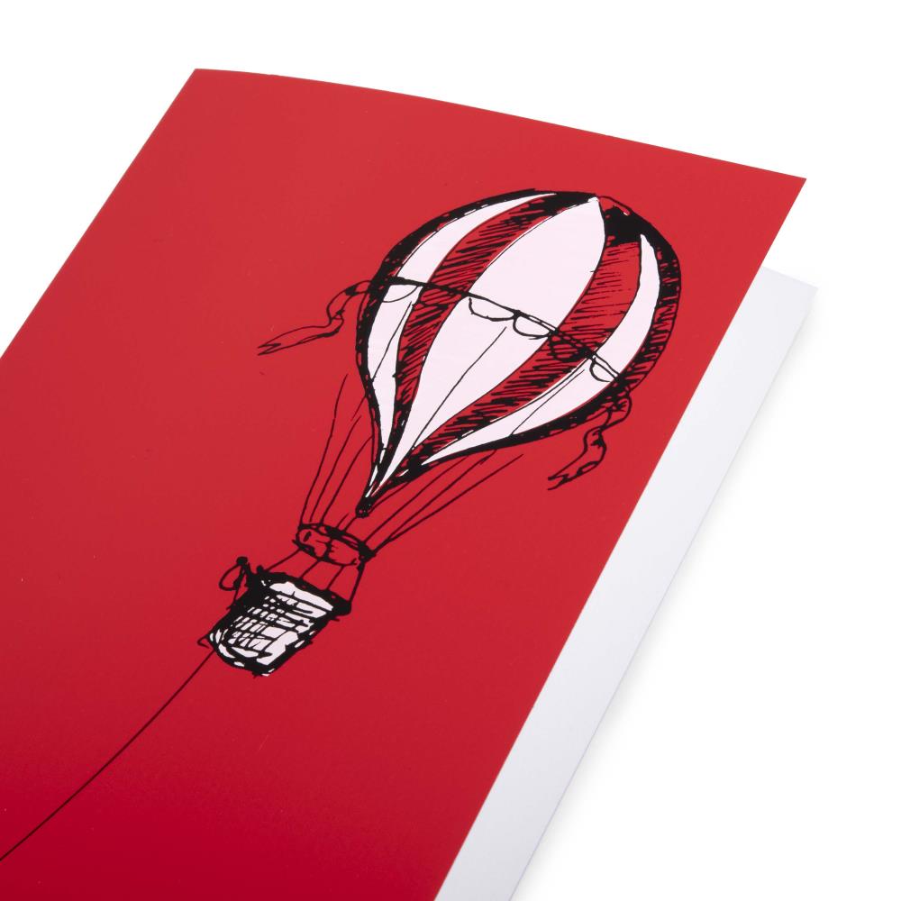 A close-up of aChristmas card with a bold red background, featuring a black illustration of a hot air balloon on the right, with a long rope extending left.