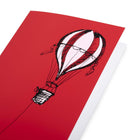 A close-up of aChristmas card with a bold red background, featuring a black illustration of a hot air balloon on the right, with a long rope extending left.