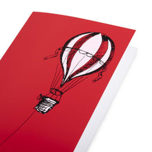 A close-up of aChristmas card with a bold red background, featuring a black illustration of a hot air balloon on the right, with a long rope extending left.