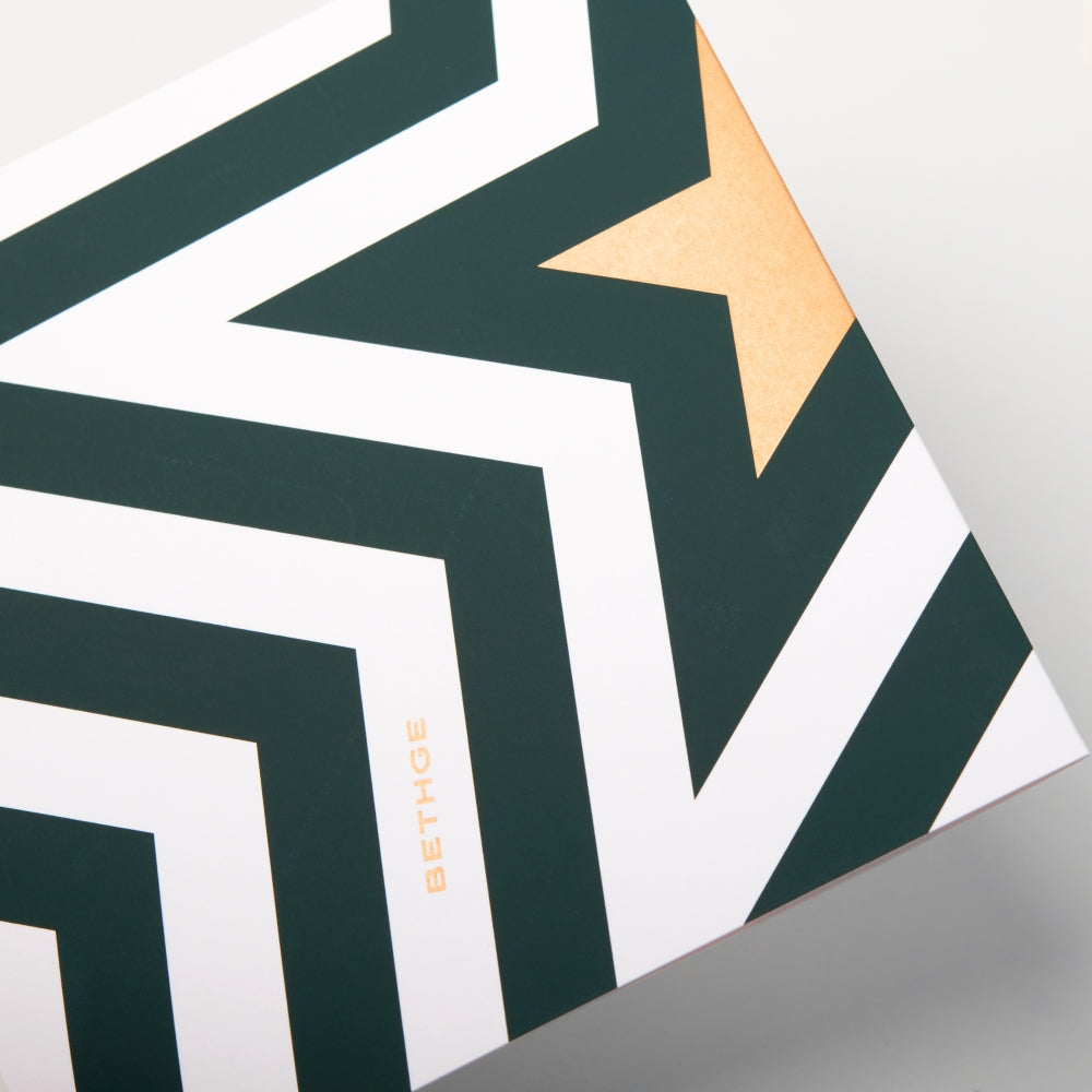 The back of a Christmas card featuring a bold zigzag pattern in dark green and white with a golden star forming a stylized Christmas tree, with the text "Bethge".