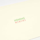 A close-up of a minimalist cream-colored Christmas card with the words 'HOHOHO' in green and 'HIHIHI' in red printed in the center.