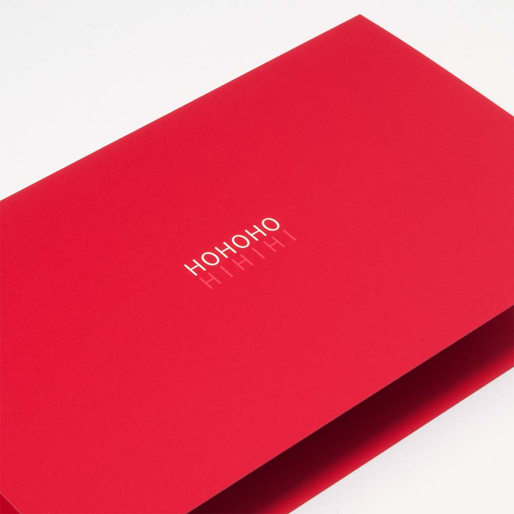 A close-up of a bright red Christmas card with the text 'HO HO HO HI HI HI' in metallic white lettering.