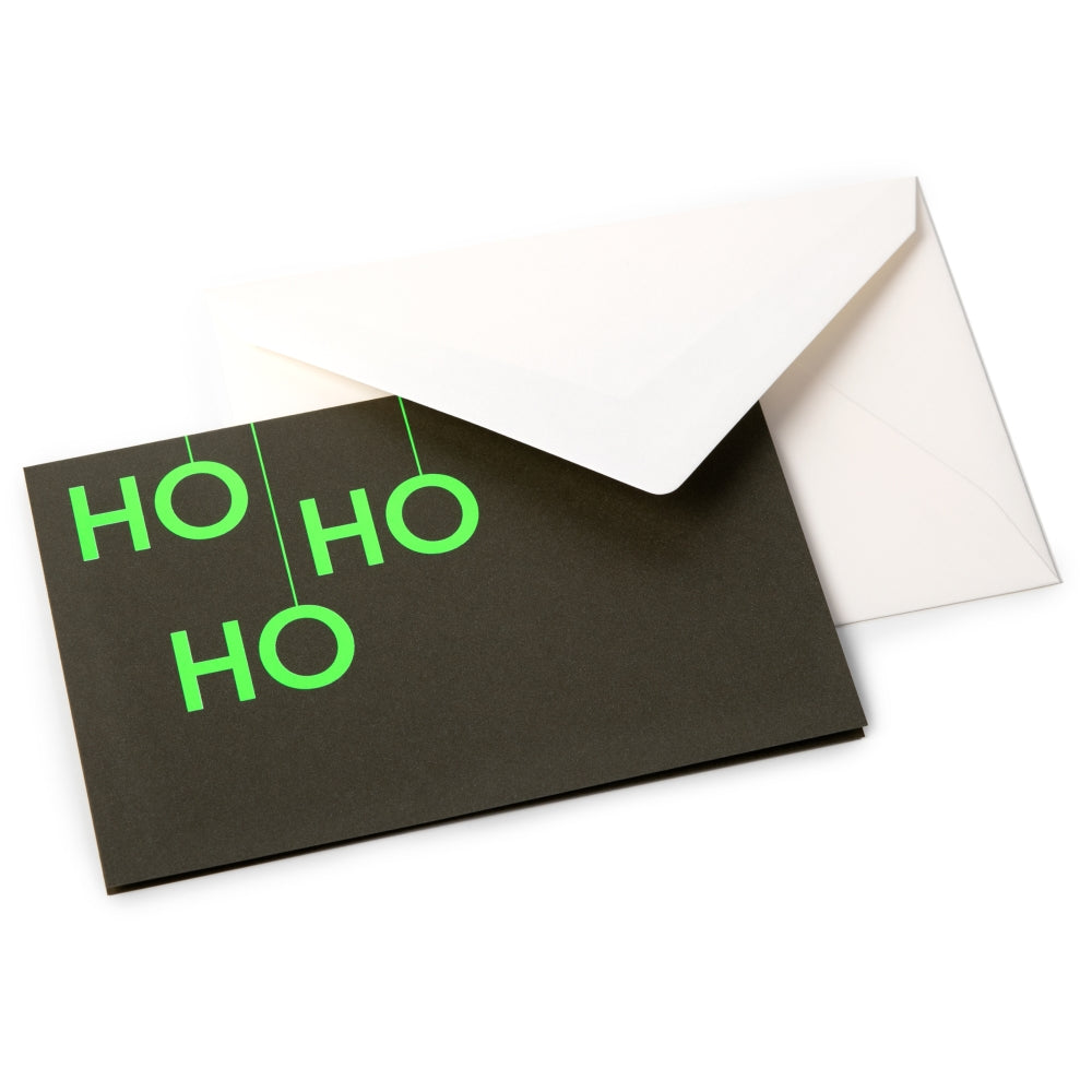 A black Christmas card with bold neon green letters arranged vertically to read "HO HO HO," paired with a white envelope.