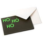 A black Christmas card with bold neon green letters arranged vertically to read "HO HO HO," paired with a white envelope.