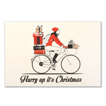 A cream-colored Christmas card featuring an illustration of a woman in a red hat and coat riding a bicycle stacked with presents, with more gifts in the front basket, and the text "Hurry up it's Christmas" in black at the bottom.