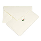 A cream-colored Christmas card with deckled edges, featuring a small holly sprig with green leaves and red berries in the center, shown with a matching cream envelope.