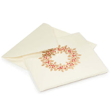 A cream-colored Christmas card with deckled edges, featuring a festive holly wreath design made of gold leaves and bright red berries, shown with a matching cream envelope.