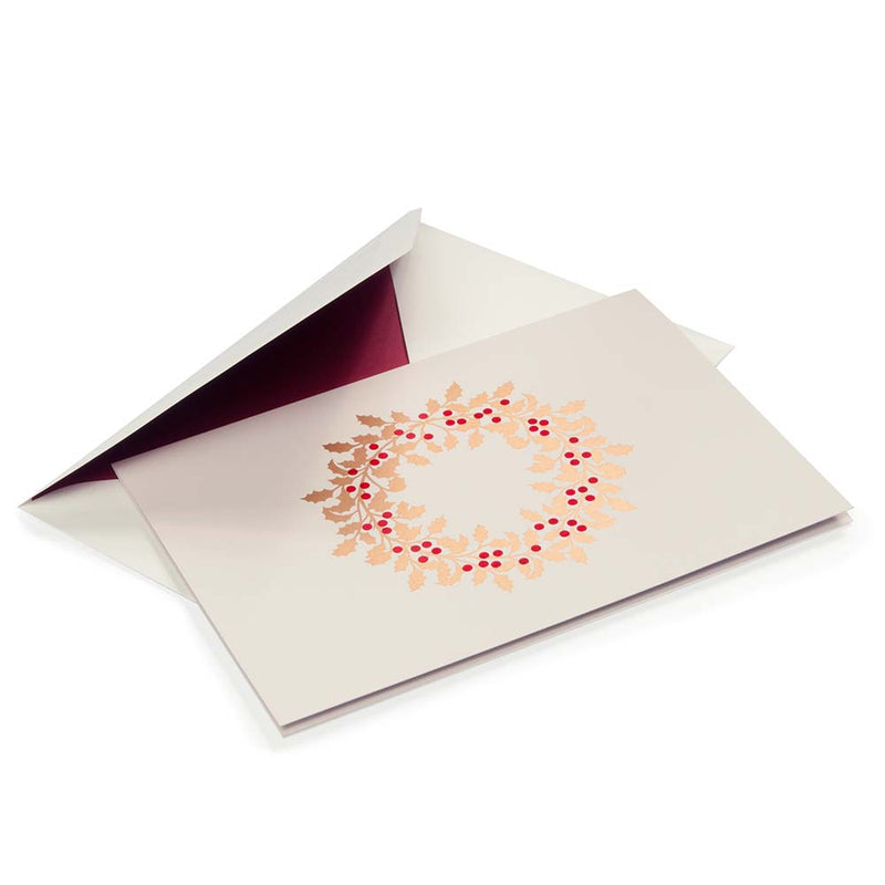 Beige Christmas card adorned with a golden holly wreath and red berries, paired with a cream envelope lined in deep burgundy.