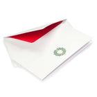 White Christmas card featuring a green holly wreath with red berries, paired with a white envelope lined in bright red.