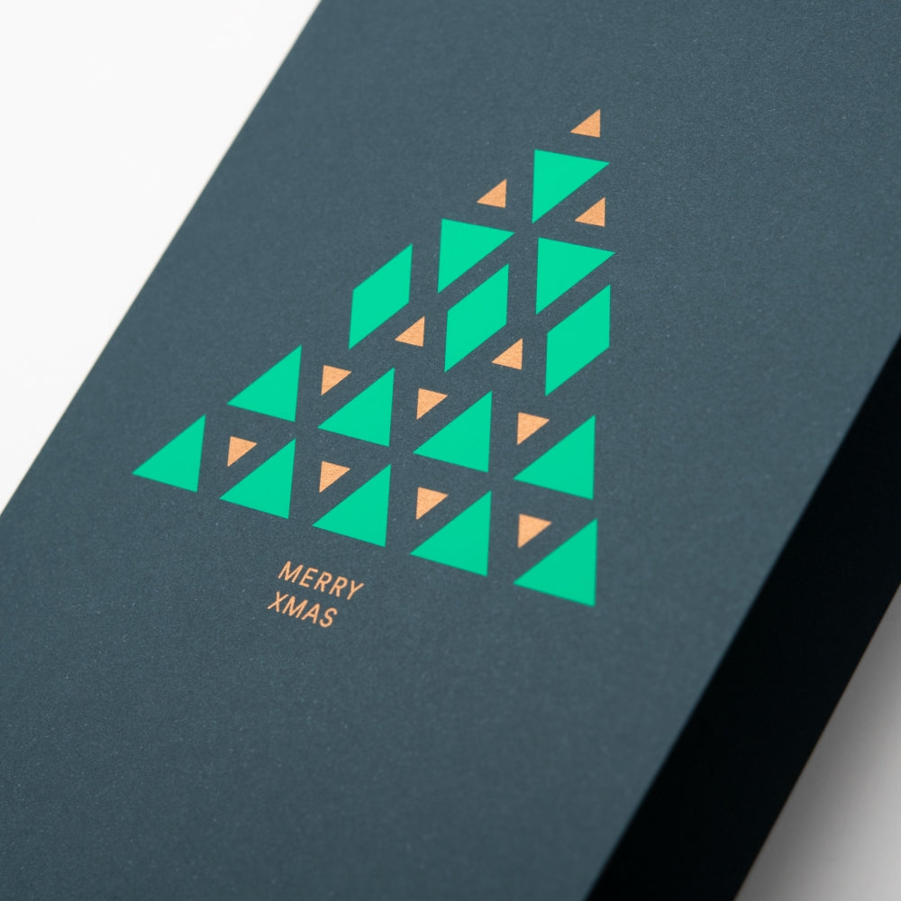 A close-up of a modern dark green Christmas card with a geometric Christmas tree design made of green and gold triangles, reading "Merry Xmas" in gold.