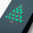 A close-up of a modern dark green Christmas card with a geometric Christmas tree design made of green and gold triangles, reading "Merry Xmas" in gold.
