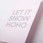 A close-up of a light pink Christmas card with bold silver text reading 'LET IT SNOW HOHO'.