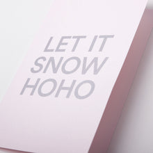 A close-up of a light pink Christmas card with bold silver text reading 'LET IT SNOW HOHO'.