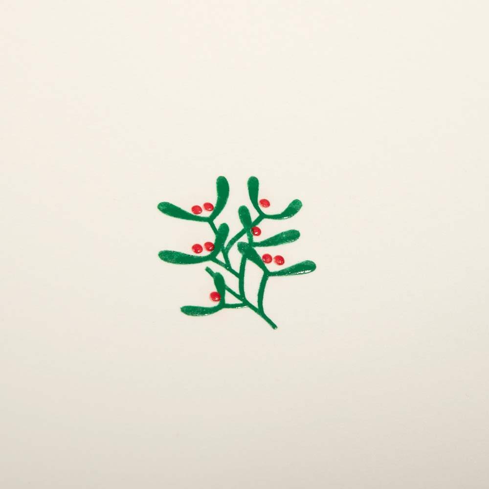 A close-up of a cream-colored Christmas card with a small mistletoe sprig of green leaves and red berries in the center.