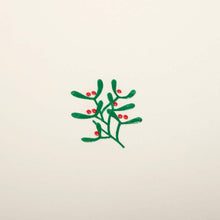 A close-up of a cream-colored Christmas card with a small mistletoe sprig of green leaves and red berries in the center.