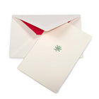 A cream-colored Christmas card with a small mistletoe sprig of green leaves and red berries in the center, shown with a cream envelope lined in bright red.